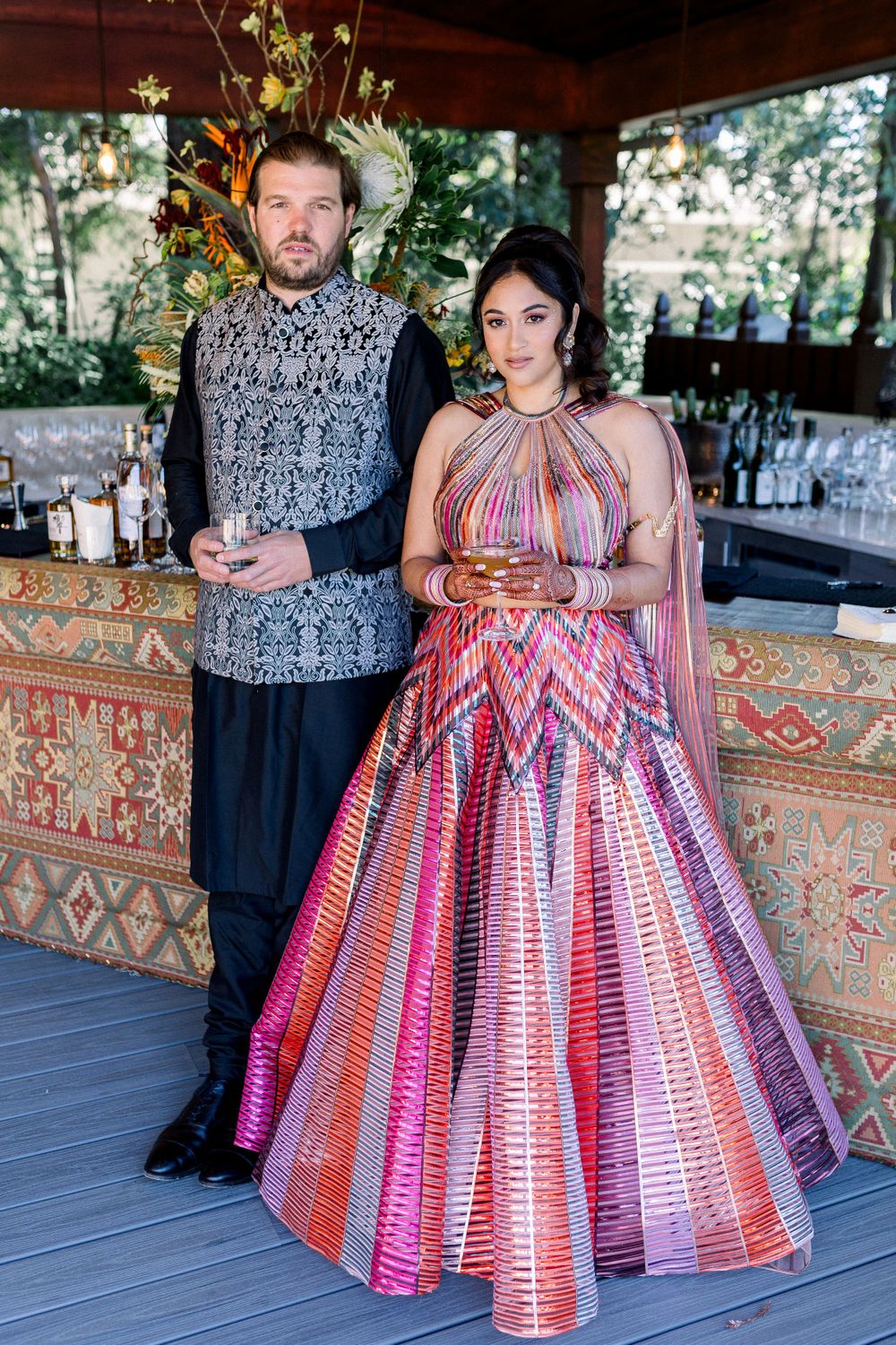An elegantly dressed couple poses for photos on a covered patio with stylish decor.