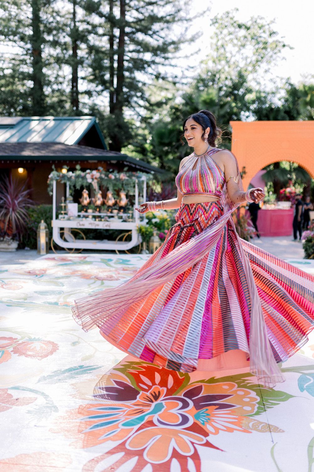 A flowing pink and white striped gown twirls against a backdrop of pine trees and outdoor party decor.