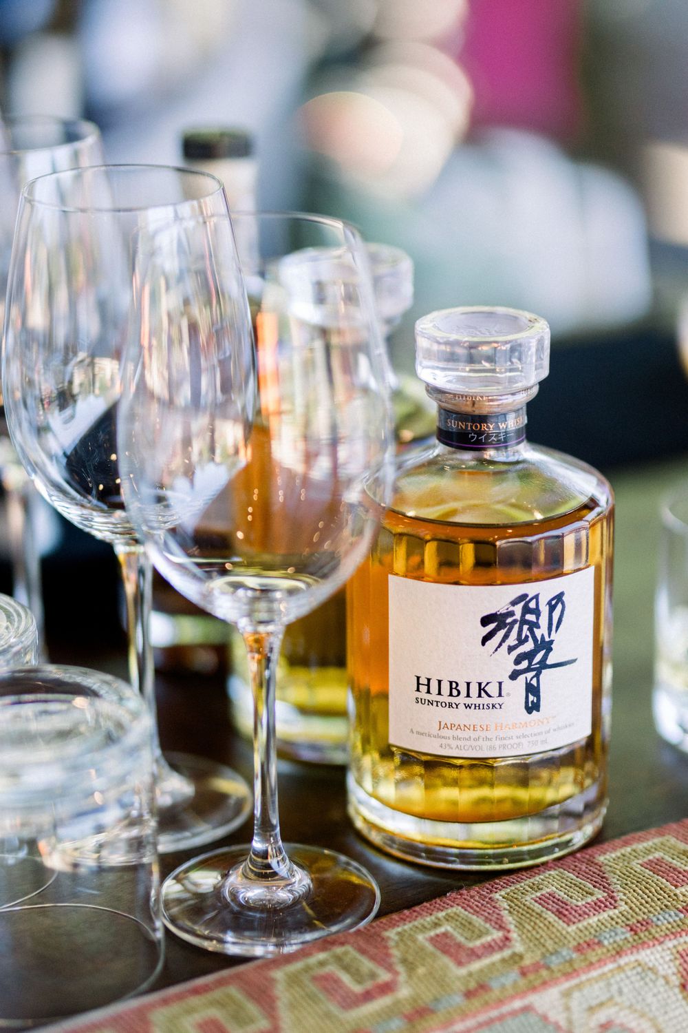 Bottles of Hibiki whiskey displayed with wine glasses on a decorative patterned table runner.