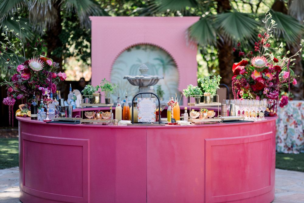 Elegant pink circular bar with floral arrangements and drink selections at a garden party.