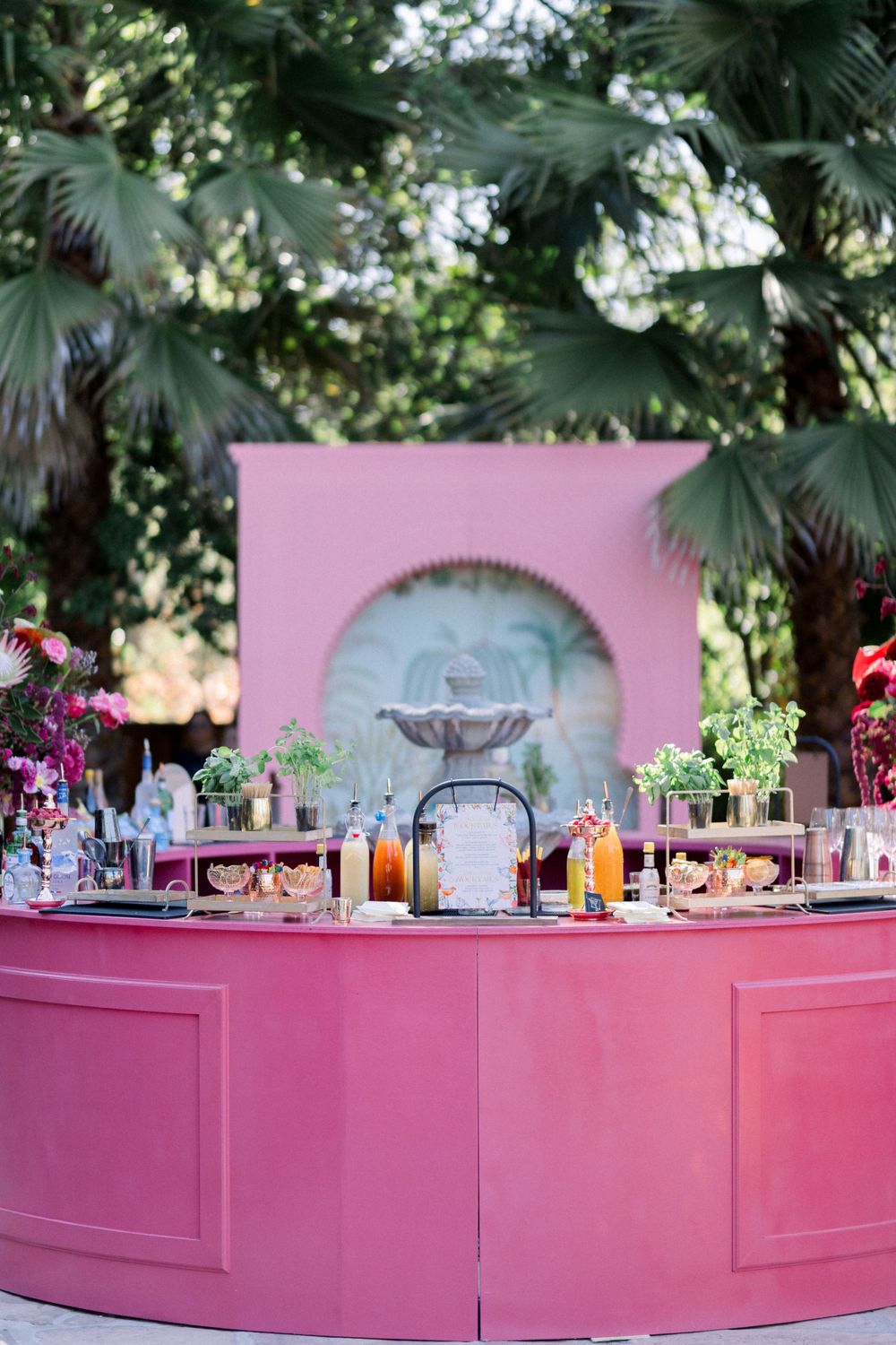 Pink circular bar setup with palm trees and colorful floral decorations at an outdoor event.