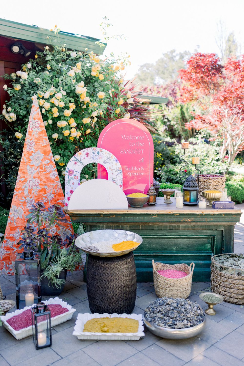 Decorative display table with pink signage, baskets and floral arrangements at an outdoor event.