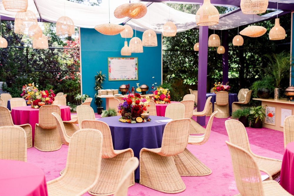 Outdoor party setup with rattan chairs and colorful table settings under hanging lanterns.