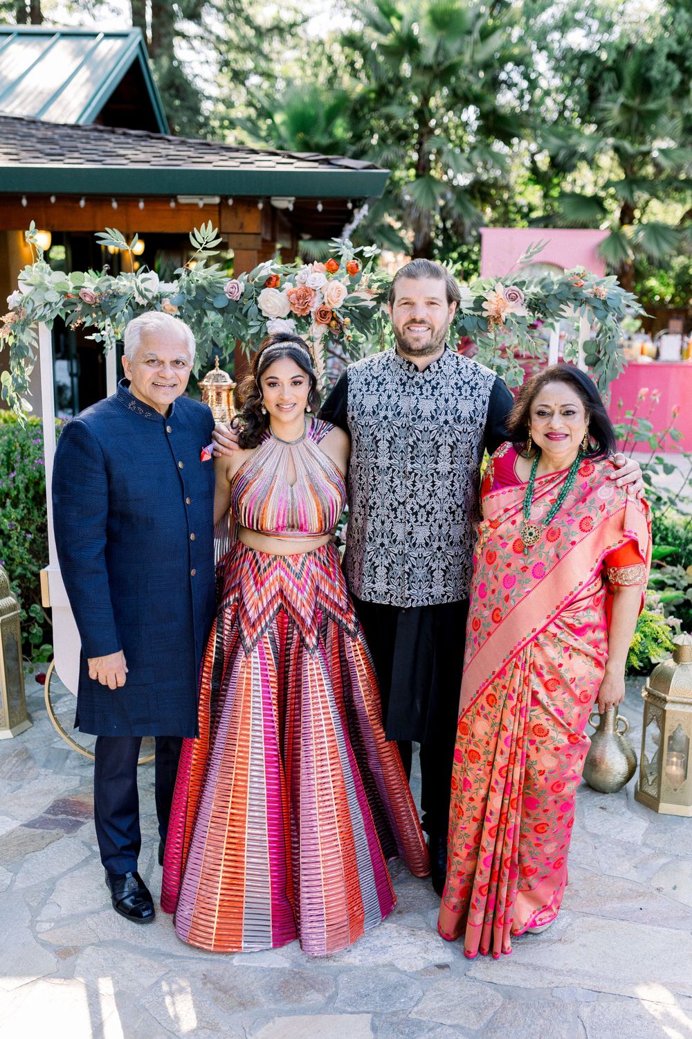 Family gathering outdoors with guests wearing colorful traditional and modern formal wear.