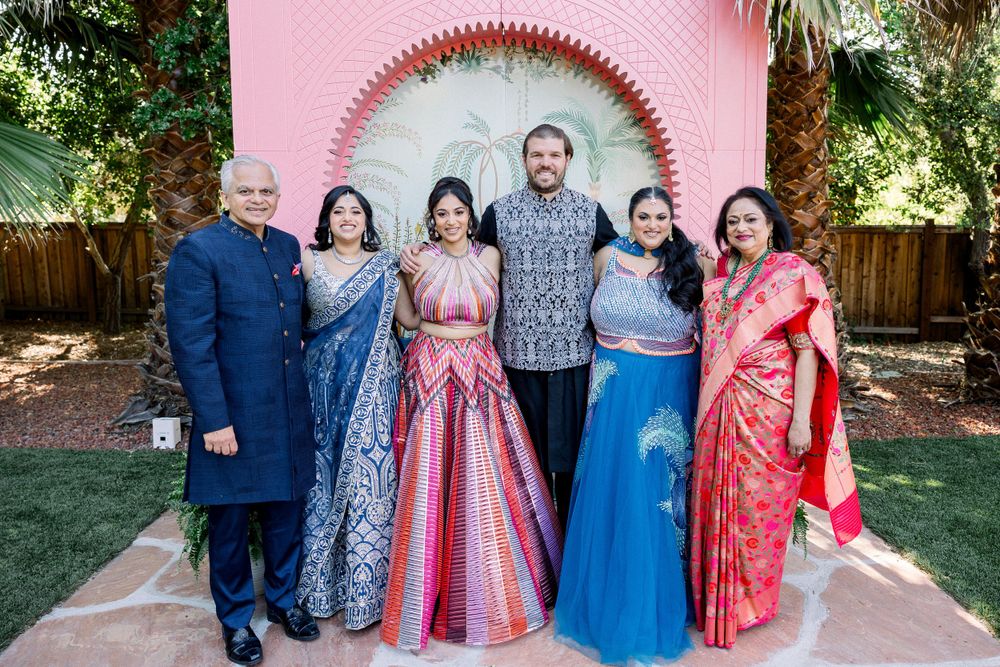 Celebration group photo with pink backdrop and guests in vibrant formal attire.