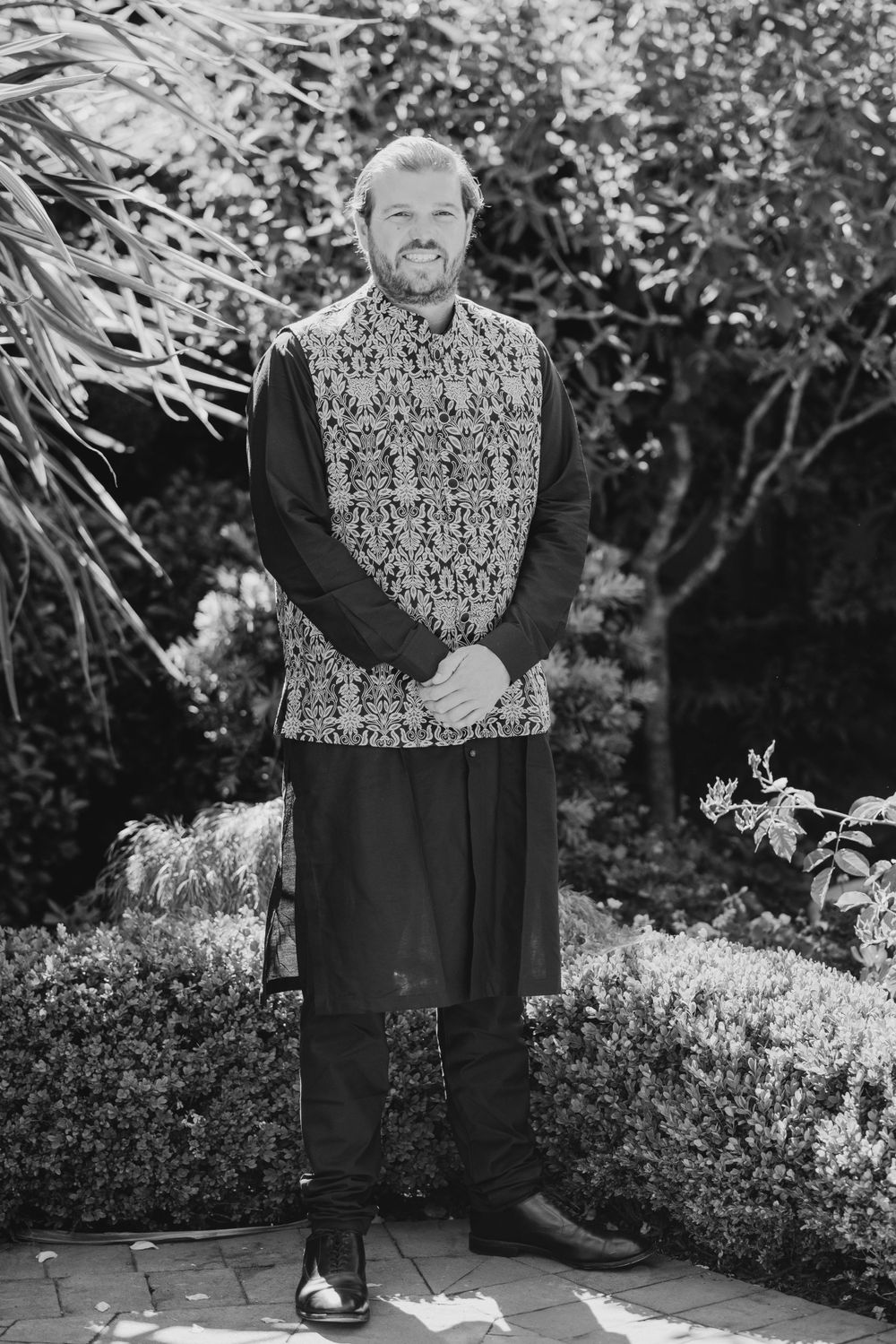 A person wearing black and white patterned vest poses in garden setting for series of black and white photos.