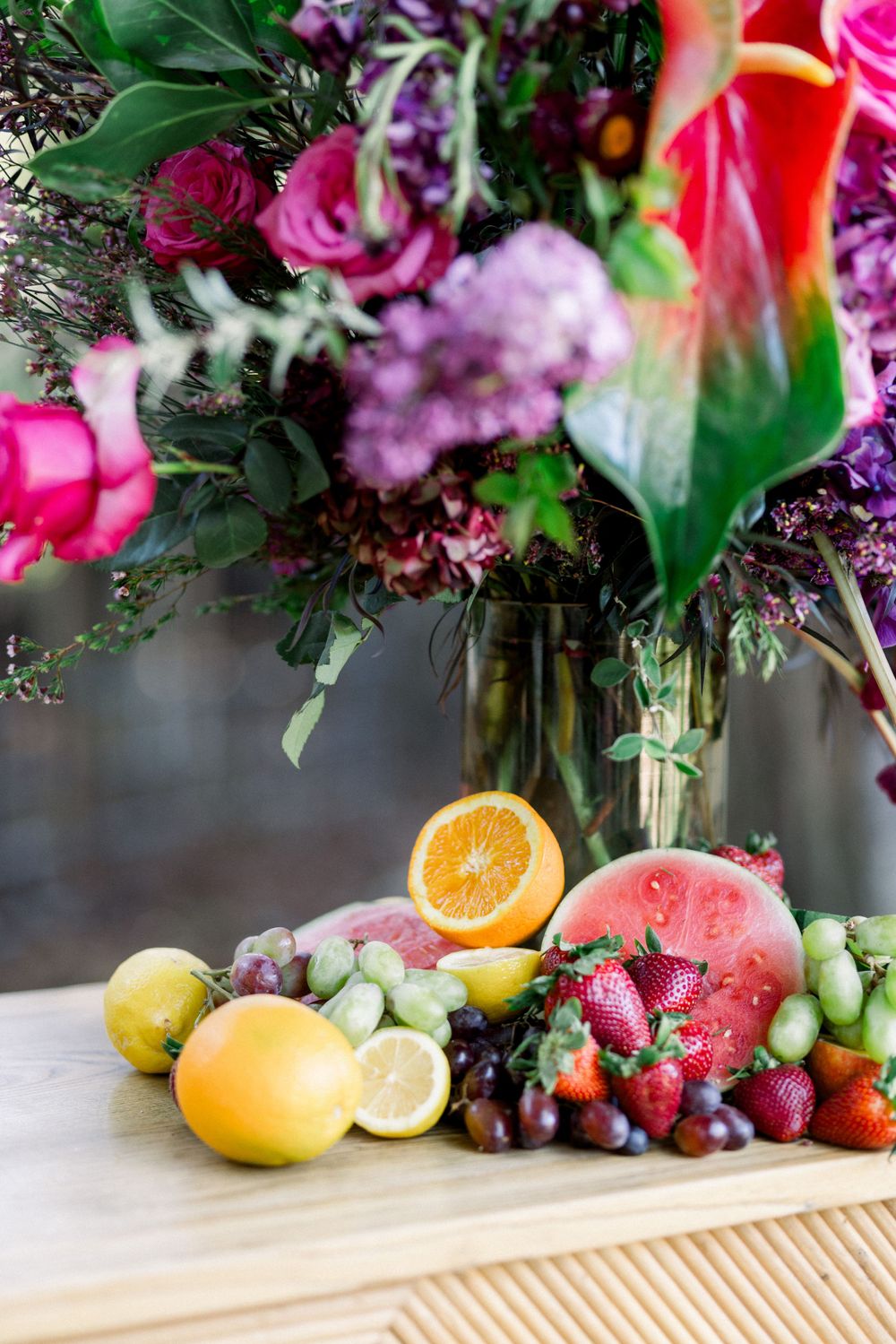 Vibrant floral centerpiece with fresh fruits and colorful blooms on a wooden surface.