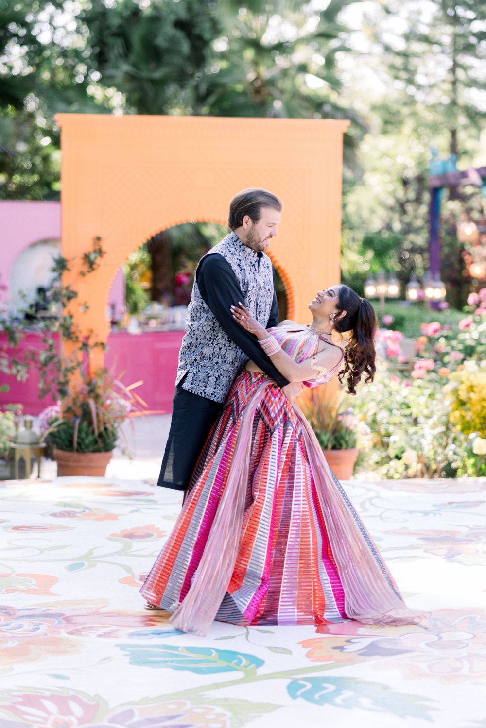 Couple dancing on a painted outdoor patio surrounded by pink walls and greenery.