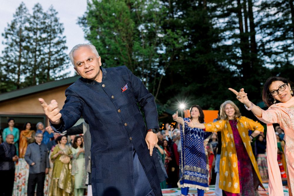 Wedding guests dance and celebrate at an outdoor reception with trees in the background.