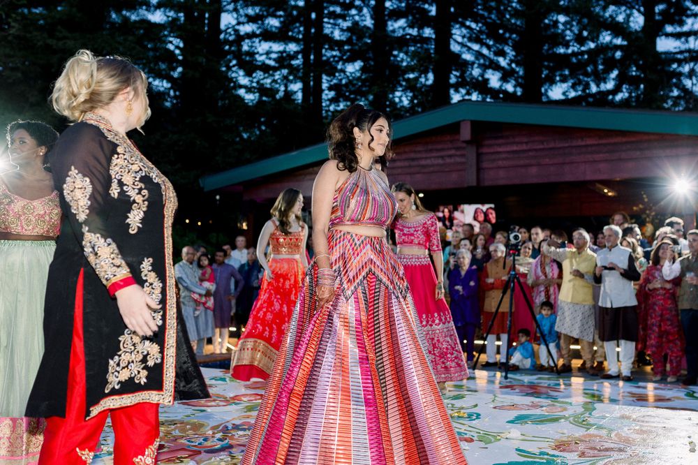 Wedding celebration with guests in vibrant formal attire dancing under tall pine trees.