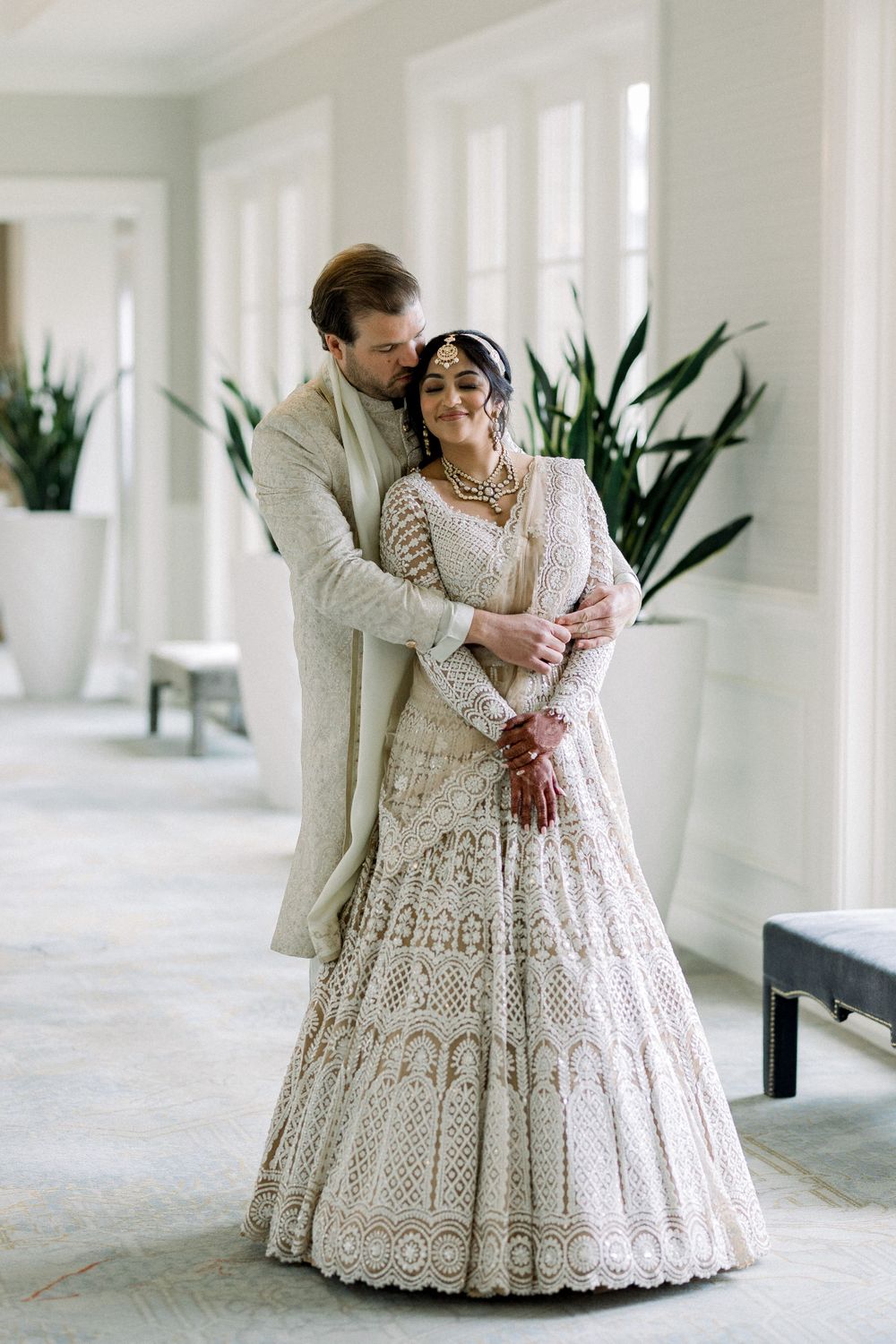Wedding couple shares intimate moments in a bright white hallway with plants.