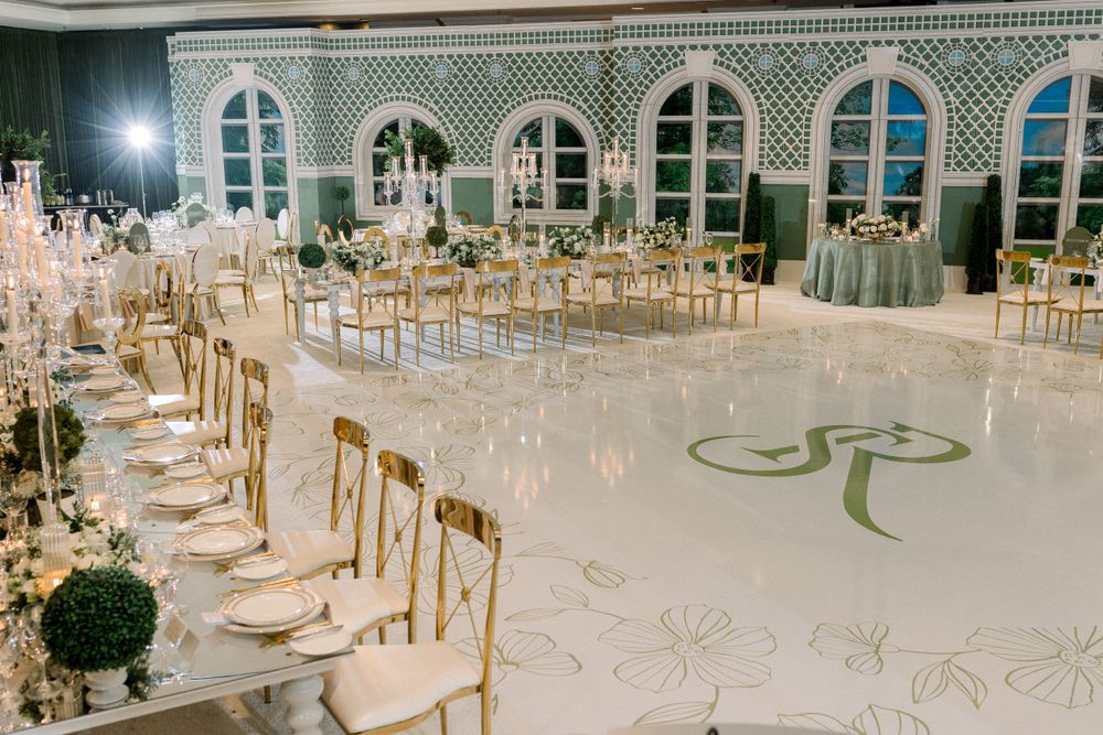 Elegant wedding reception venue with ornate windows and gold chairs arranged around a white dance floor with monogram design.
