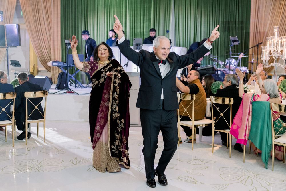 Wedding guests dancing joyfully at reception with green curtain backdrop.