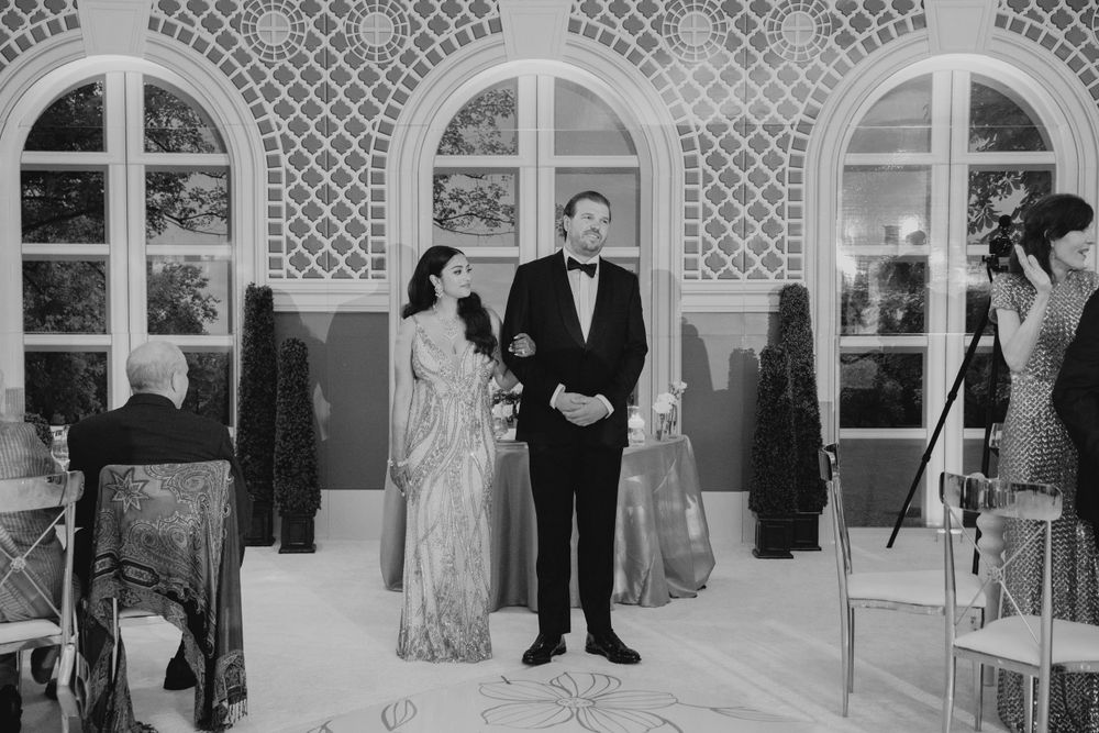 Black and white photo of wedding ceremony in front of arched windows and lattice backdrop.