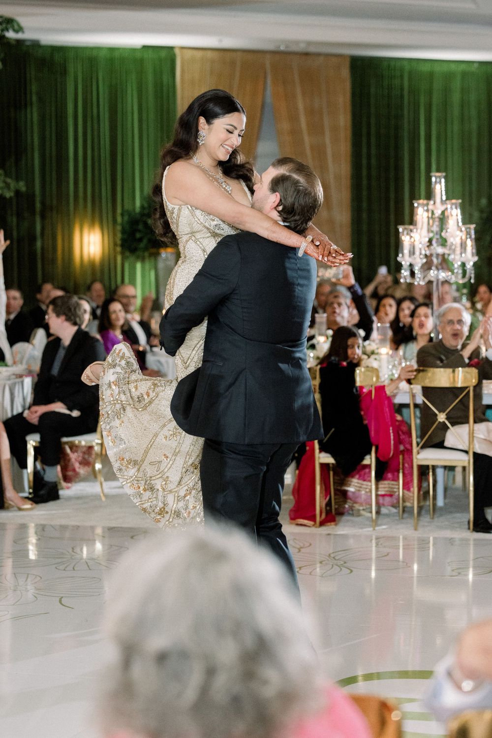 Romantic dance lift during wedding reception with chandelier lighting and green drapery backdrop.