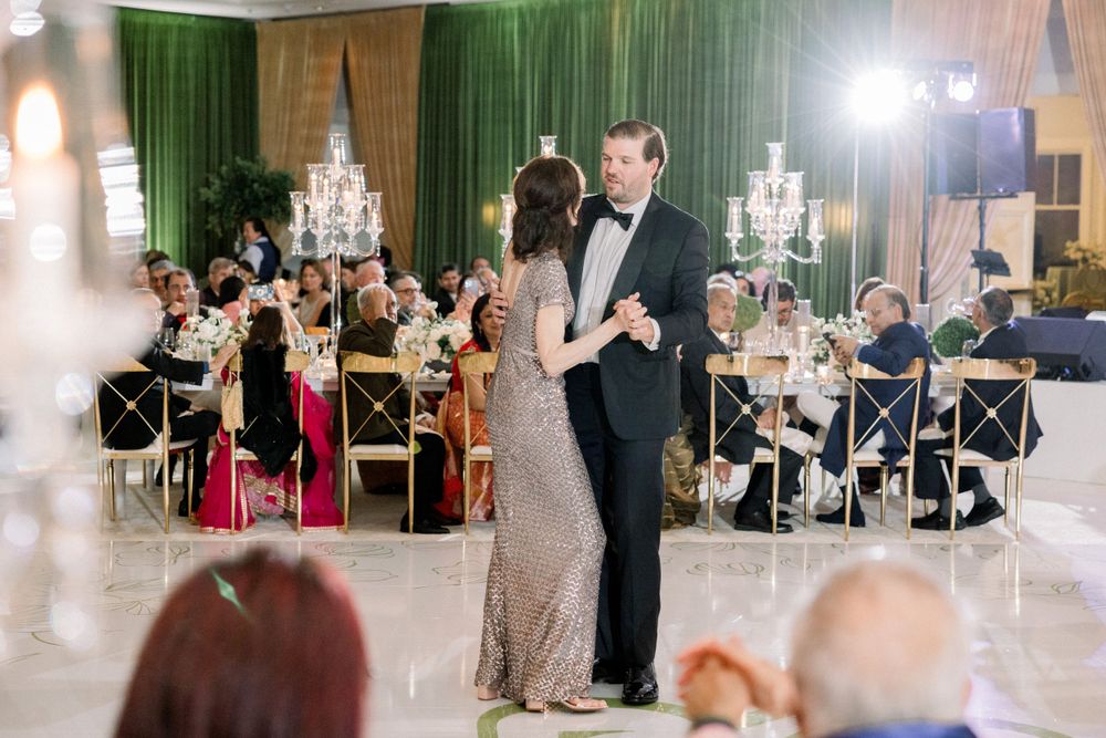 Elegant couple shares first dance at wedding reception with ornate chandeliers and green drapery.