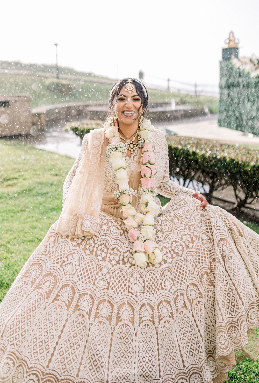 Stunning blush pink lehenga with intricate embroidery detail photographed in an outdoor garden setting.