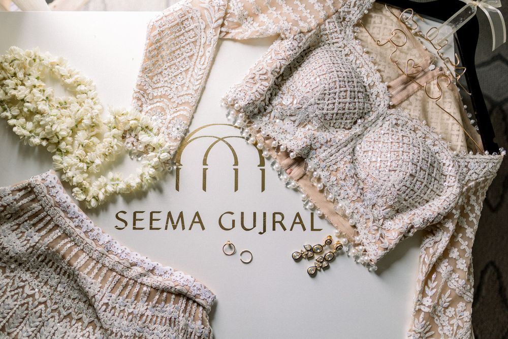 Delicate white wedding accessories including lace details, rings, and floral elements arranged on a light background.