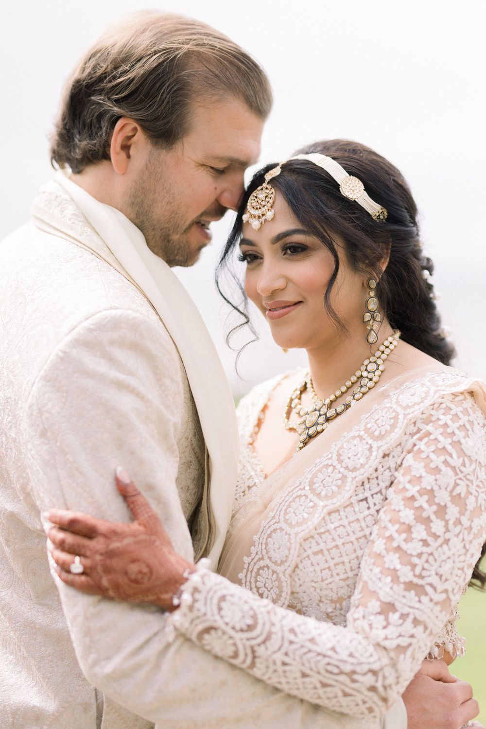 Intimate wedding moment captured in soft white tones with delicate lace and elegant jewelry details.