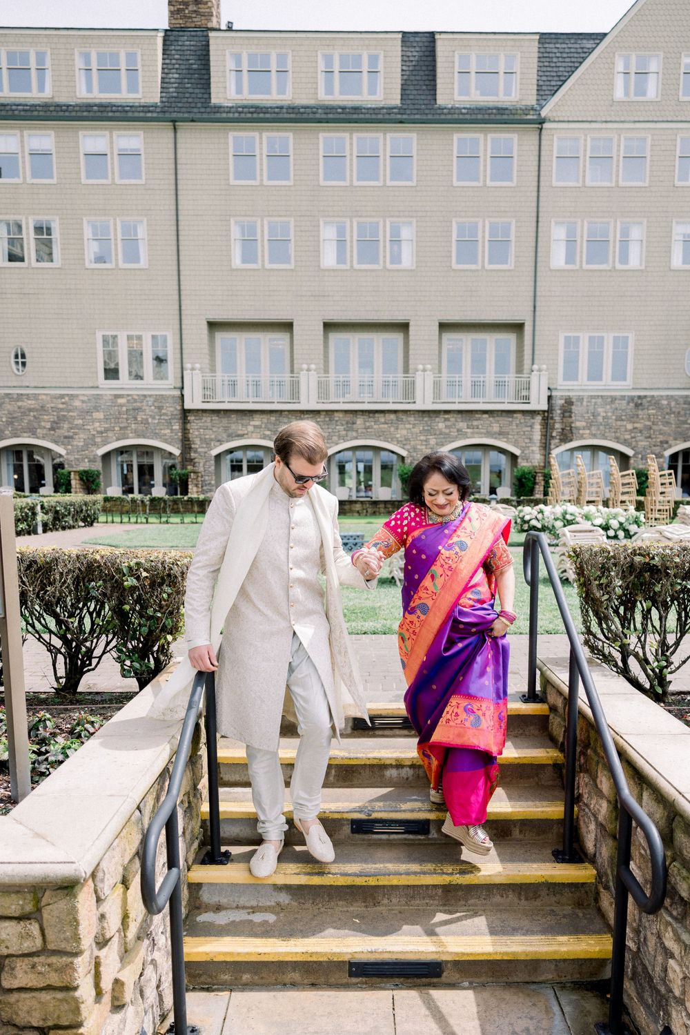 Wedding couple in white attire posing on a wooden boardwalk against a coastal resort backdrop.