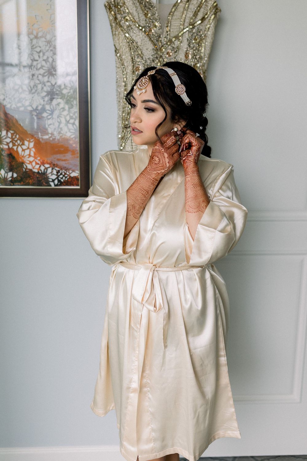 Bride in silk robe prepares for wedding day against light blue walls.
