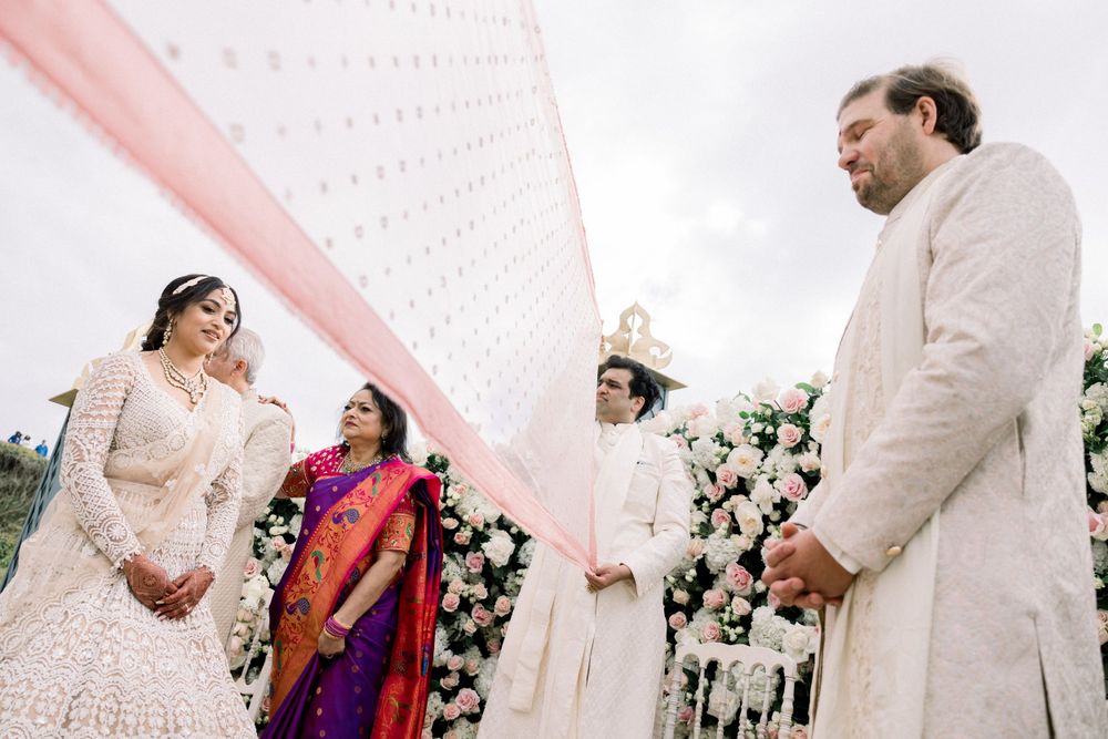 Couple in traditional wedding attire standing beneath a white canopy during ceremony.