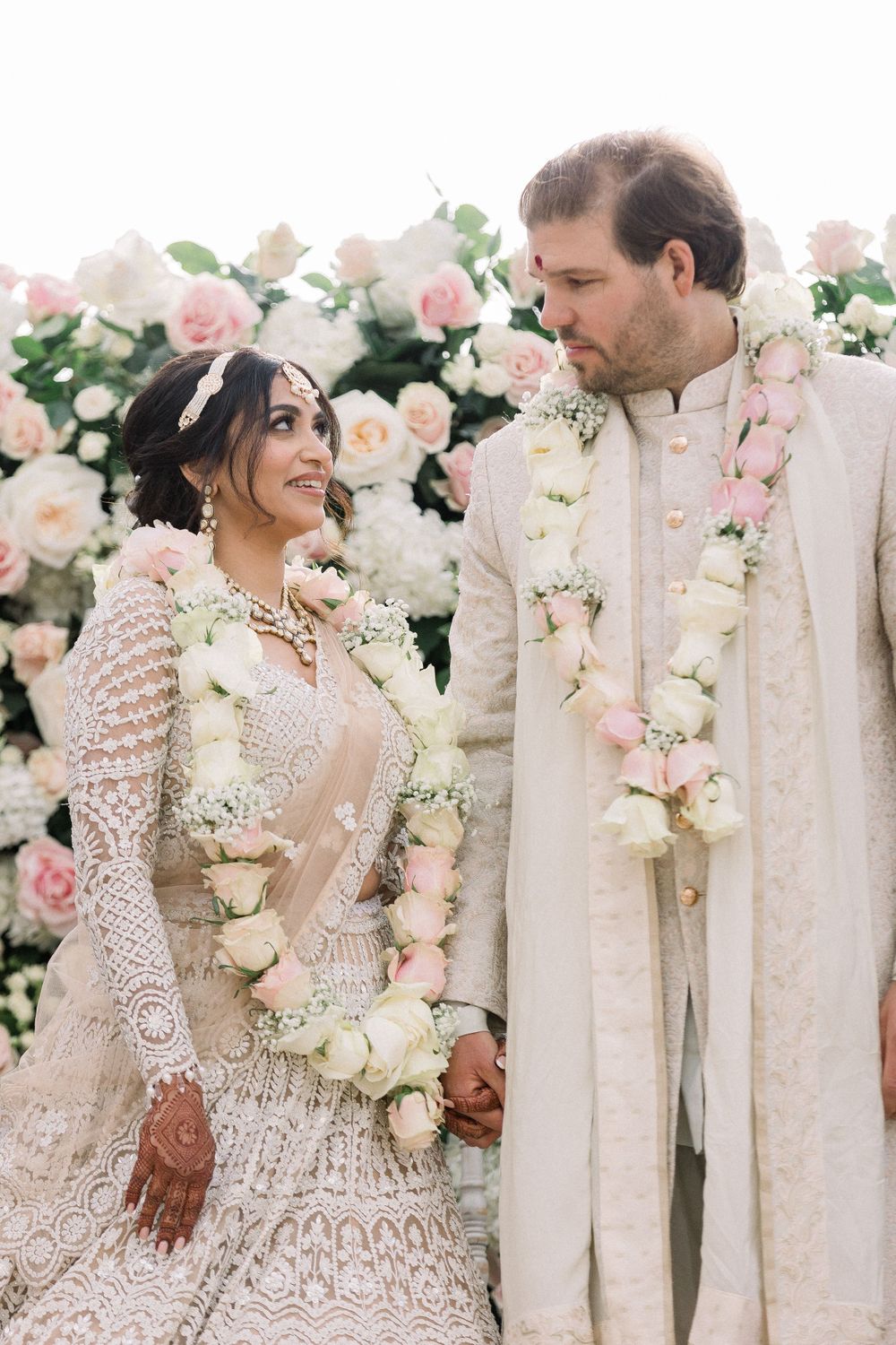 Elegant couple posing among pink and white rose arrangements at their wedding.