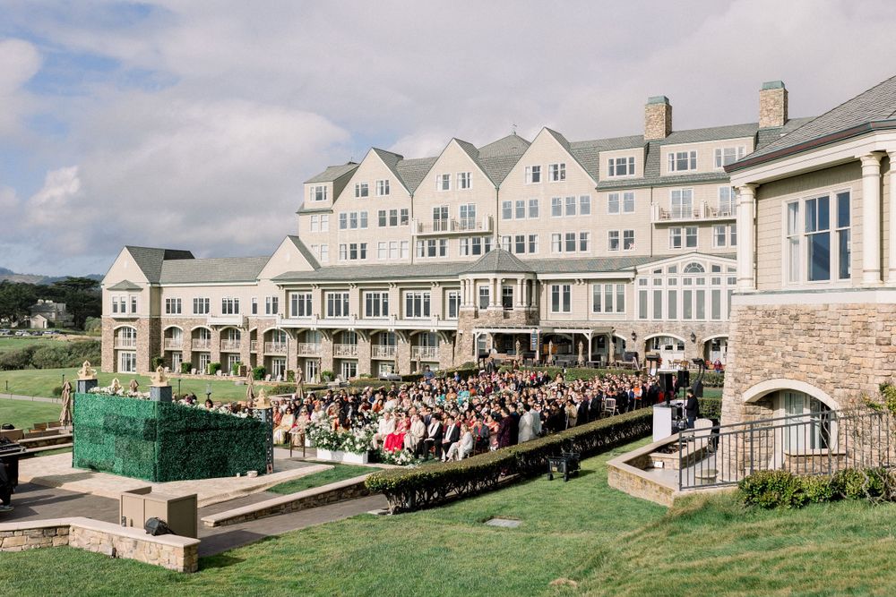 Large coastal wedding venue with guests seated on a manicured lawn overlooking the ocean.