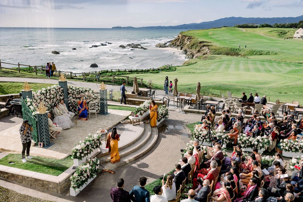 Panoramic view of an oceanside wedding venue with green lawns and gathered guests.