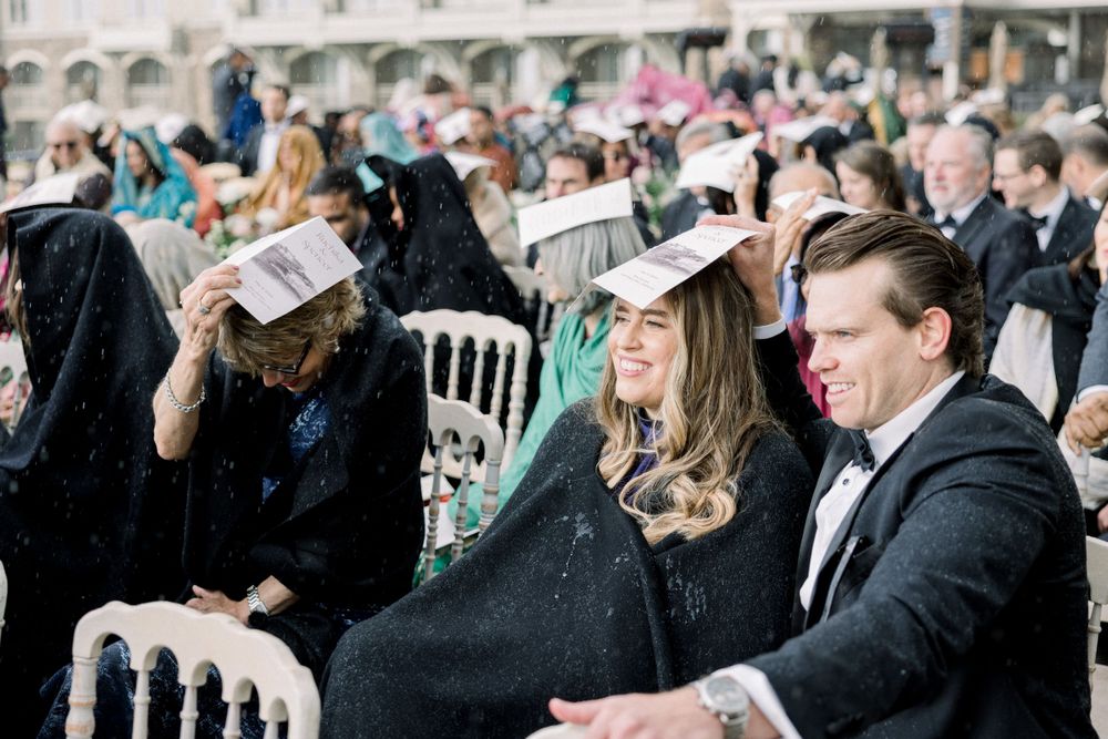 Wedding guests seated in rows of white chairs during outdoor ceremony.