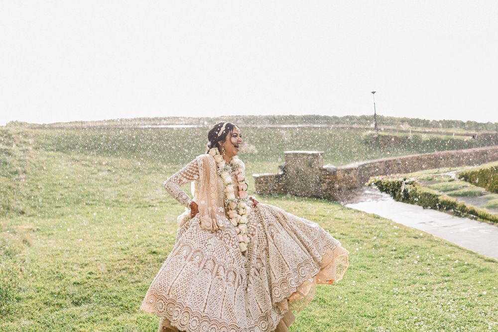 Bride wearing ornate beaded gown twirls in outdoor garden setting.