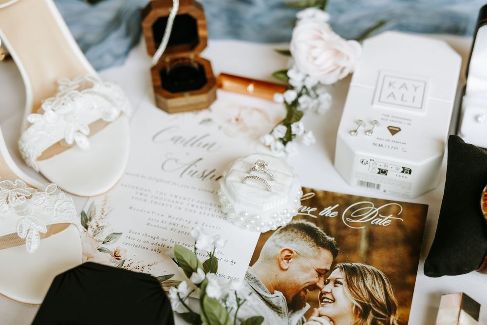 Wedding details arranged on white table showing invitation cards, rings, flowers, and ethereal decor elements in natural light.