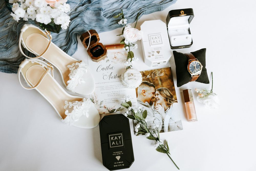 Flatlay composition of wedding stationery with rings, perfume bottles, and dried flowers in neutral beige tones.