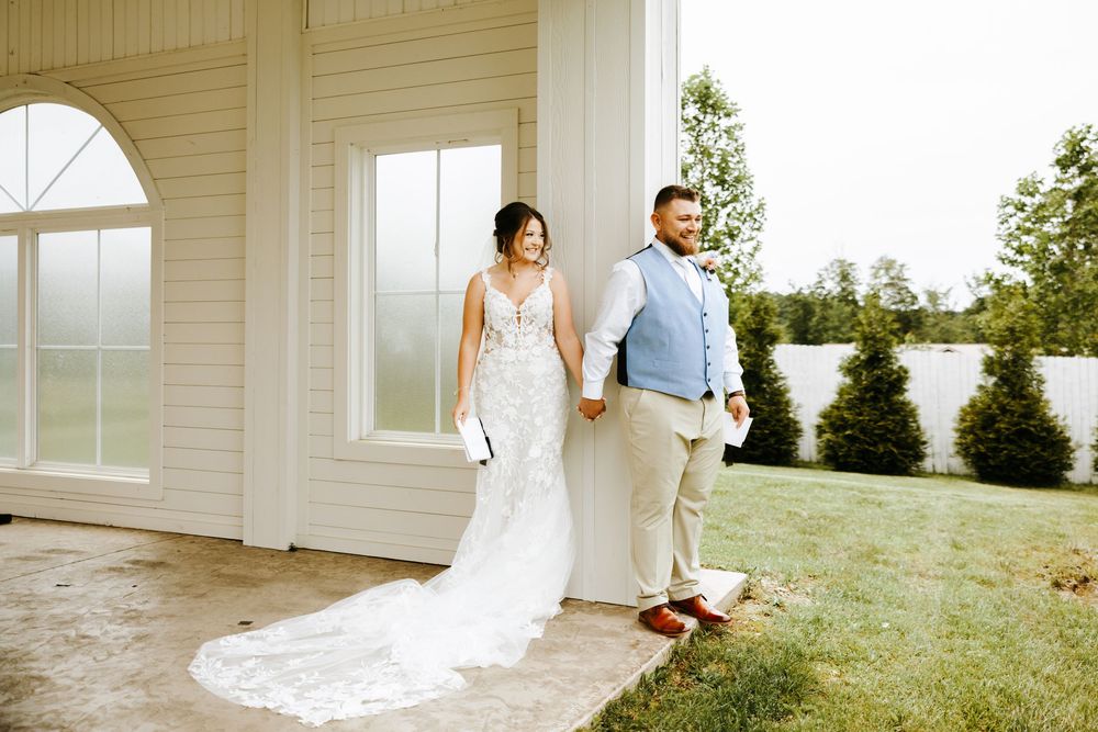 A couple standing together at a white wedding venue with a flowing bridal gown and garden backdrop.