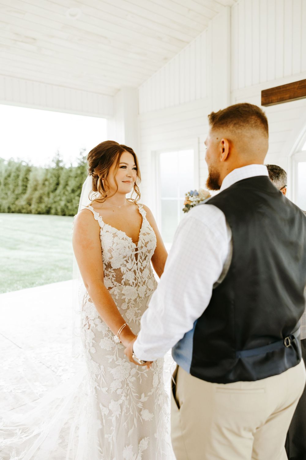 A tender moment between figures in a light-filled indoor setting wearing wedding attire.