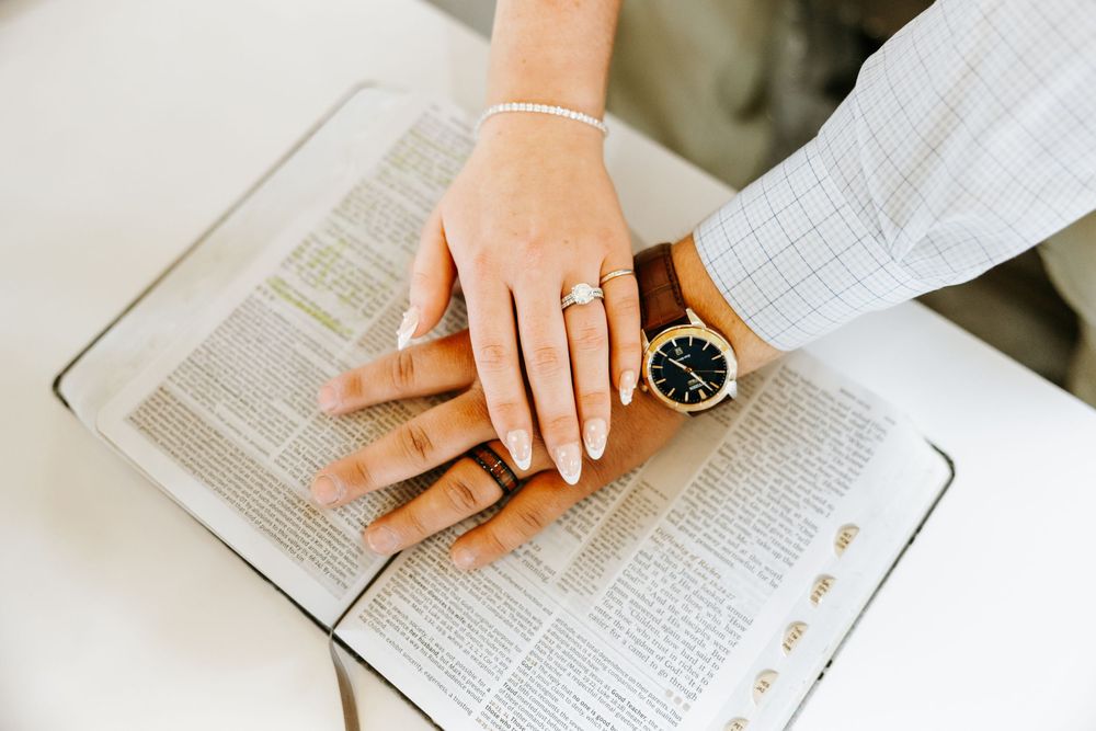 Hands resting on open book pages with black wristwatch visible on desk during reading or study session.