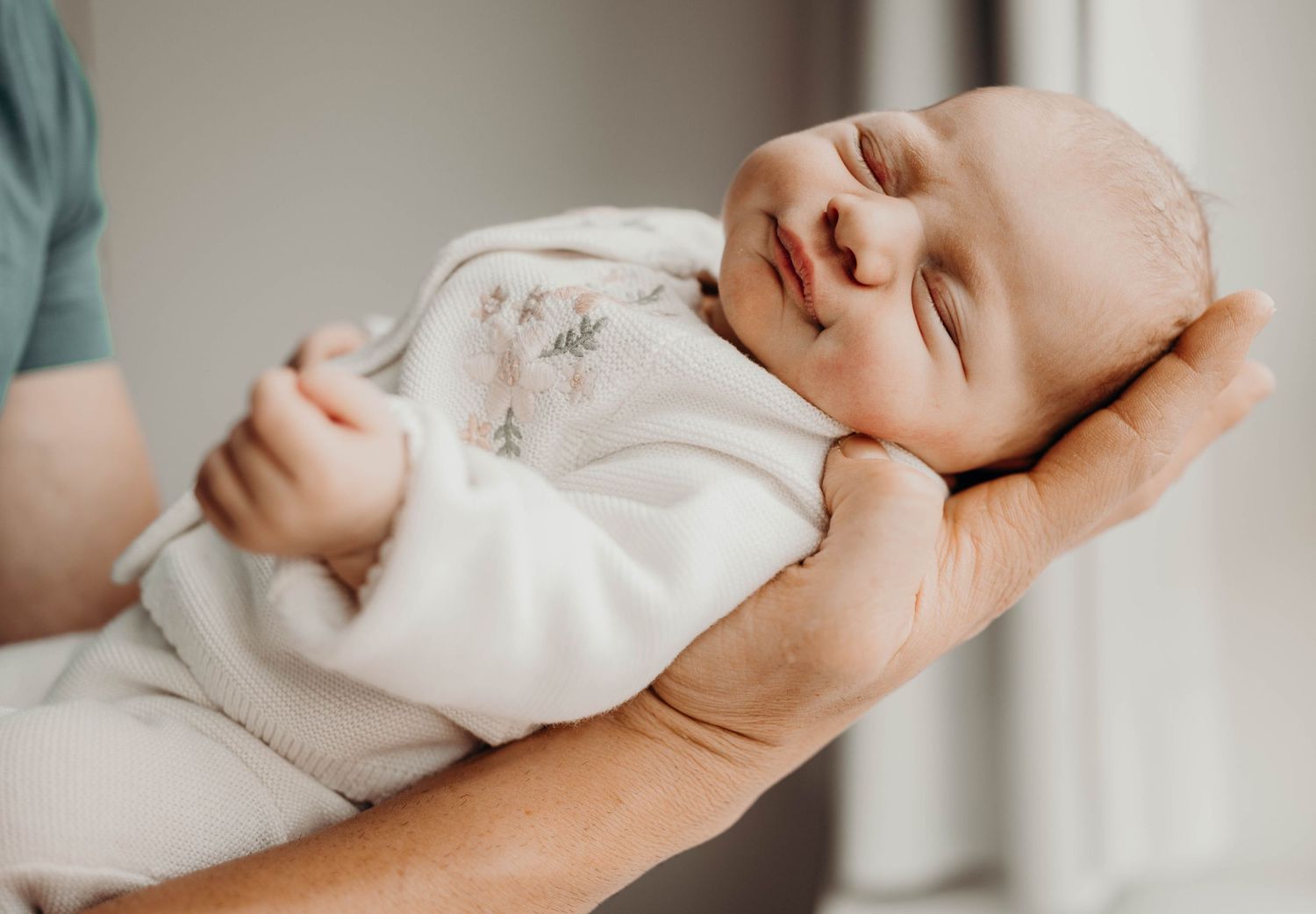 A content newborn baby sleeping peacefully while being held in caring hands.