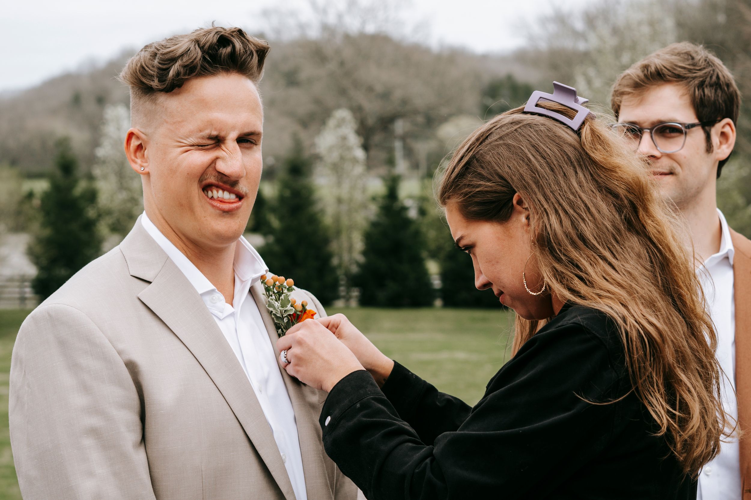 A boutonniere being pinned on a light beige suit at an outdoor event.
