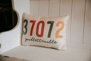 A decorative white pillow with zipcode numbers in earth tones spelling out Millersville.