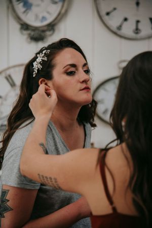 A getting-ready moment with someone having earrings adjusted, with vintage clocks on wall.