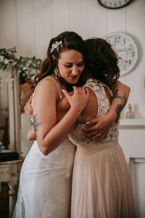 Two people sharing an emotional embrace in formal attire against a white wall with clocks.