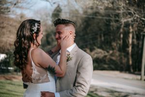Couple shares tender moment outdoors in elegant wedding attire with natural backdrop.