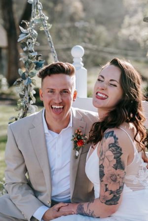 Happy couple laughing together on vintage swing during wedding photoshoot.