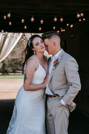 An intimate wedding portrait under string lights with the couple in white dress and beige suit.