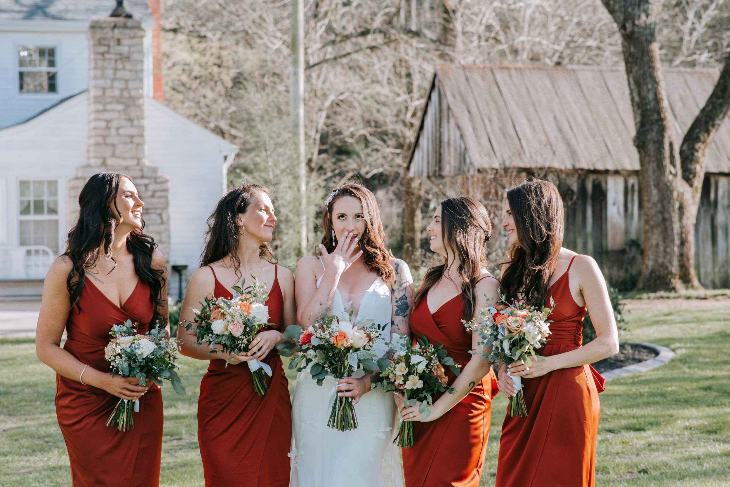 Bridal party in deep red dresses sharing candid laughter moment outdoors.