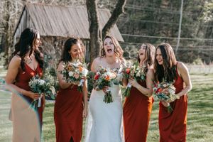 Wedding party wearing burgundy bridesmaid dresses standing together outdoors with floral bouquets.