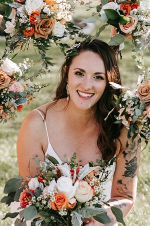Floral arch frames wedding portrait with roses and greenery in outdoor garden setting.
