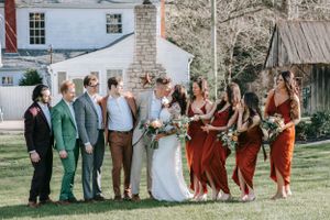 Wedding party in burgundy and green attire poses together on lawn in front of historic building.