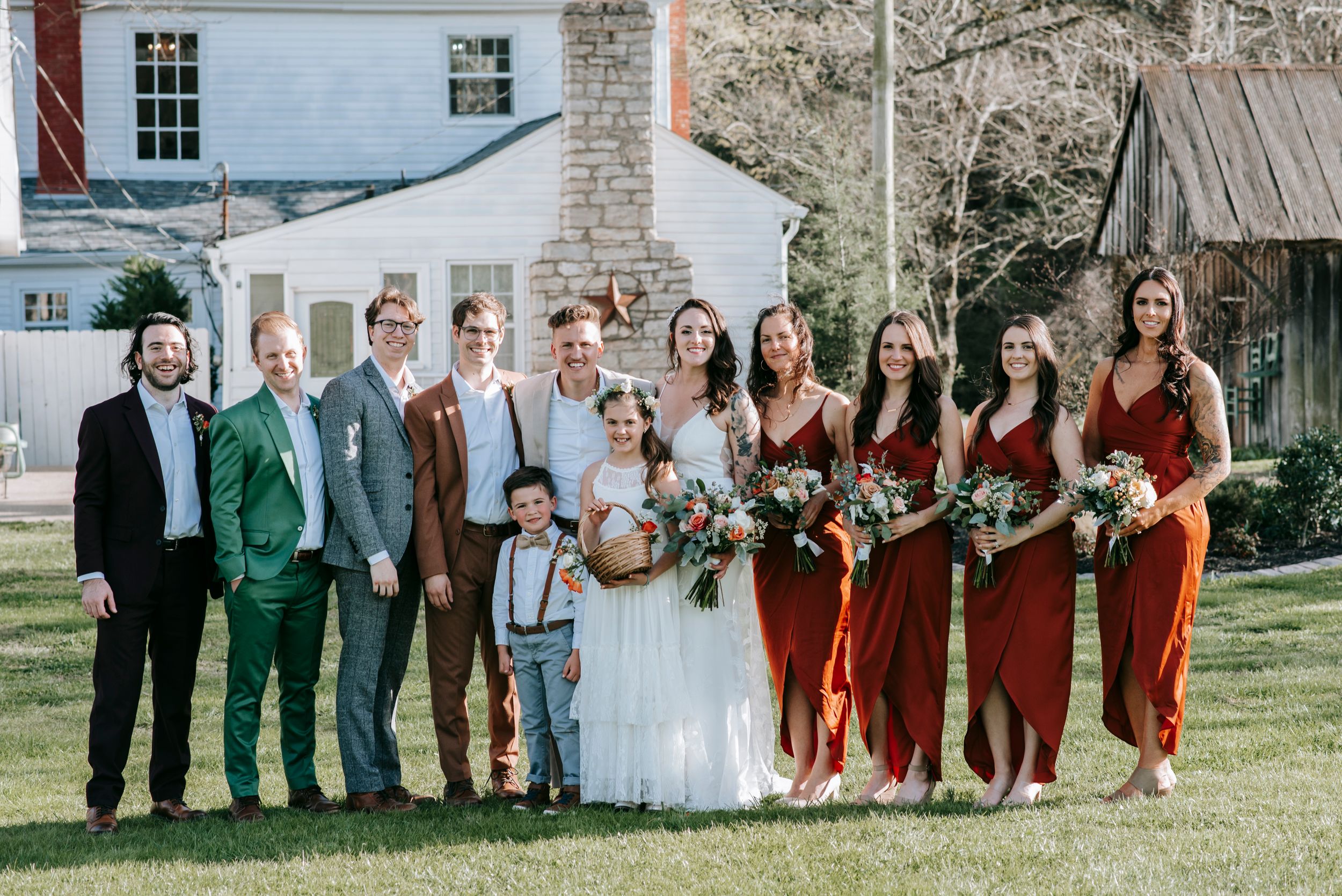 Full wedding party including groomsmen and bridesmaids poses together outdoors.