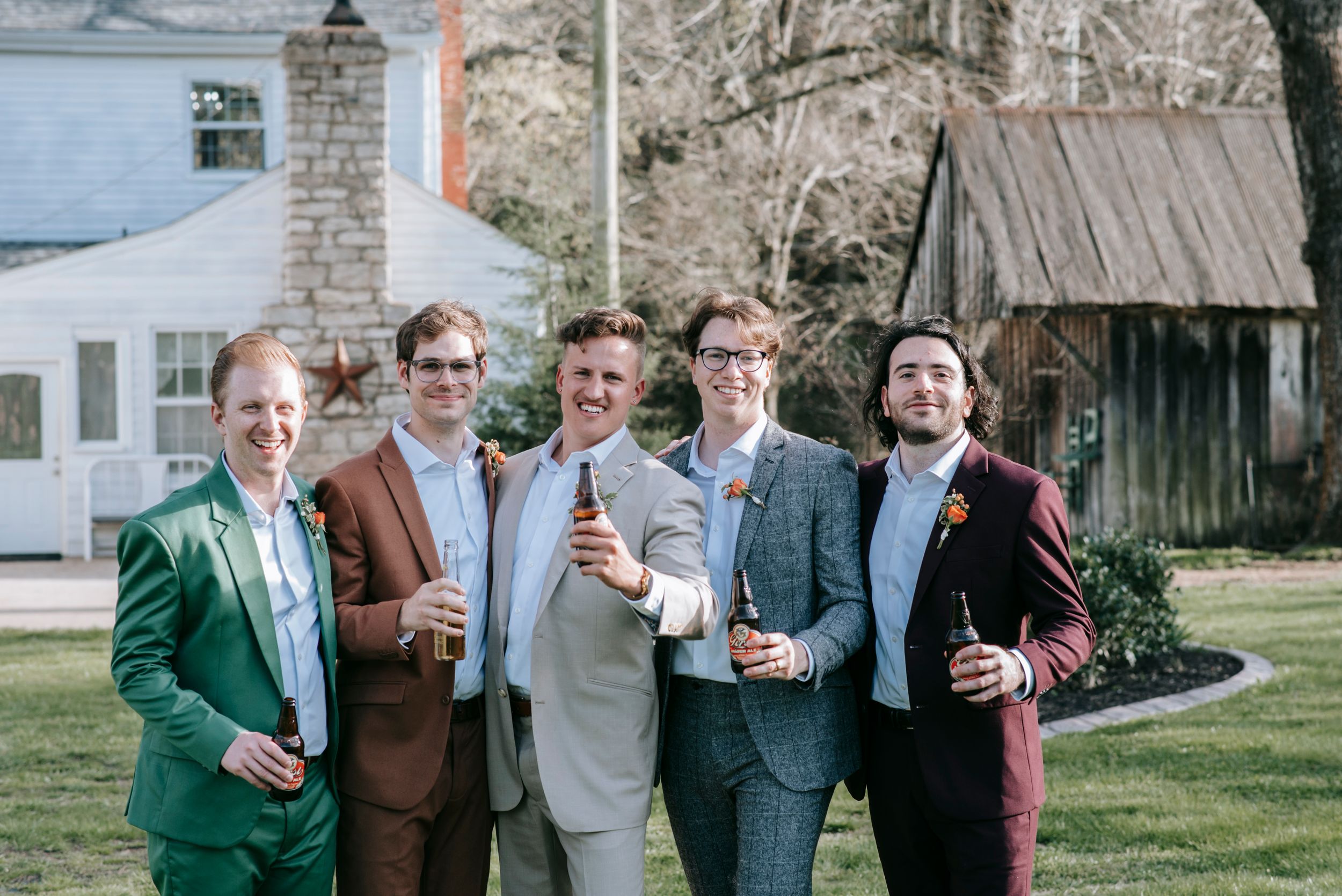 Groomsmen in colorful suits posing together on lawn during wedding celebration.